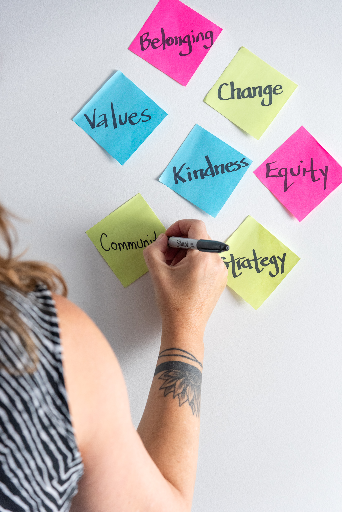 A person writing meaningful words on sticky notes posted on a wall.